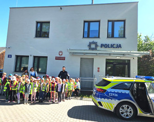 Grupa przedszkolaków z policjantem przed budynkiem komisariatu