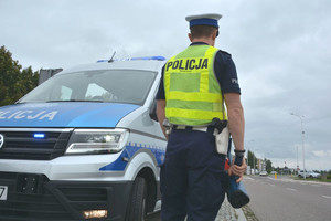 Policjant z radarem w ręku obok radiowozu podczas służby na drodze