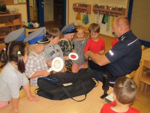 Policjant w sali przedszkolnej zapoznaje dzieci z wyposażeniem służbowym