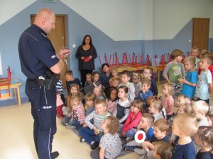 Policjant w przedszkolu prezentuje dzieciom wyposażenie do służby