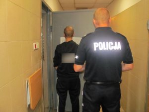 Policjant z jednym z zatrzymanych mężczyzn w pomieszczeniu dla osób zatrzymanych