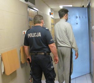 Policjant z jednym z zatrzymanych mężczyzn przed celą