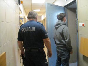 Policjant z jednym z zatrzymanych mężczyzn przed celą