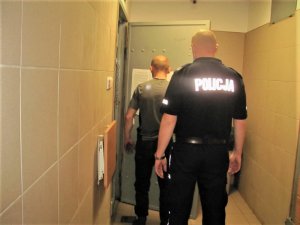 Policjant z jednym z zatrzymanych mężczyzn przed celą