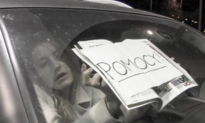 kobieta z kartką na szybie samochodu z napisem POMOCY