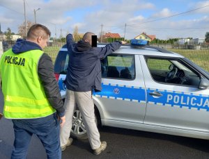 Policjant z zatrzymanym mężczyzną przy radiowozie