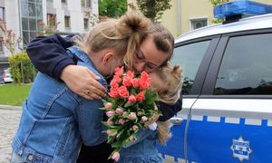 Policjantka z kwiatami i dziećmi przy radiowozie