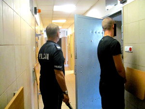 Policjant z jednym z zatrzymanych mężczyzn przed celą