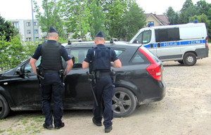 dwóch policjantów sprawdza samochód na parkingu