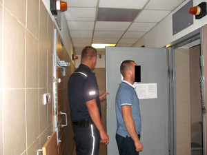 Policjant z jednym z zatrzymanych mężczyzn przed celą
