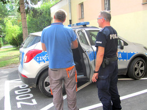 Policjant z zatrzymanym mężczyzną przy radiowozie