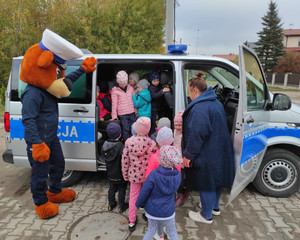 Policyjny miś i nauczycielka z dziećmi przy radiowozie