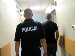 Policjant z jednym z zatrzymanych mężczyzn przed celą