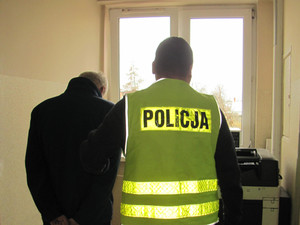 Policjant z zatrzymanym mężczyzną stoją na korytarzu komendy