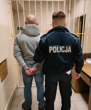 Policjant z zatrzymanym mężczyzną przed kratą w celi