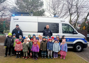 Policjant i ratownik z grupą przedszkolaków przy radiowozie