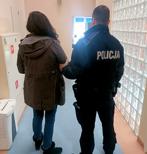 Policjant z zatrzymaną kobietą na korytarzu w budynku komisariatu