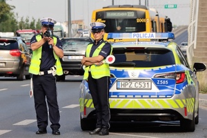 Policjanci przy radiowozie i pojazdy na drodze podczas działań