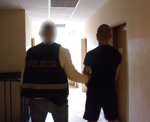 policjant operacyjny z trzyma zatrzymanego, na korytarzu jednostki