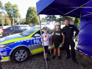 Policjant i 2 dzieci w elementach umundurowania przy radiowozie