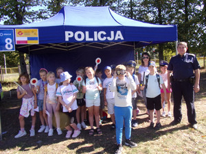 Policjant z grupą dzieci przed policyjnym stanowiskiem na pikniku
