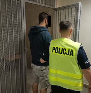 Policjant z zatrzymanym mężczyzną przed pomieszczeniem dla osób zatrzymanych