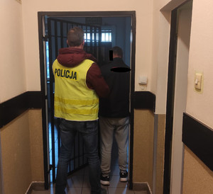 Policjant w kamizelce prowadzi zatrzymanego korytarzem