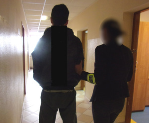 Policjantka w ubraniu cywilnym prowadzi korytarzem zatrzymanego mężczyznę