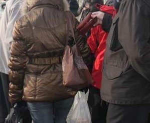 Kobieta z torebką na ramieniu, z której złodziej wyciąga portfel