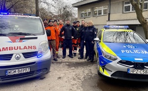 Radiowóz i ambulans oraz grupa policjantów i ratowników medycznych między nimi