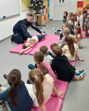 Policjant z grupą dzieci uczy udzielania pierwszej pomocy
