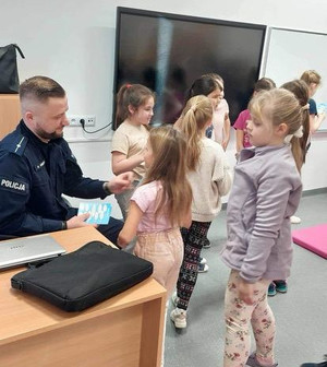 Policjant rozdaje dzieciom materiały profilaktyczne