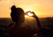 Zdjęcie kobiety z sercem z dłoni na tle słońca
