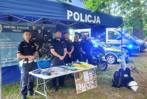 Grupa policjantów i pojazdy służbowe przy stanowisku na pikniku