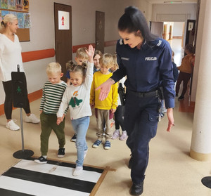 policjantka uczy grupę dzieci przechodzenia przez jezdnię w sali