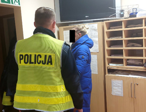 Policjant rozmawia z zatrzymaną kobietą w pokoju komendy