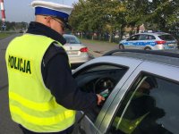 Policjant drogówki kontroluje kierowcę, w tle radiowóz