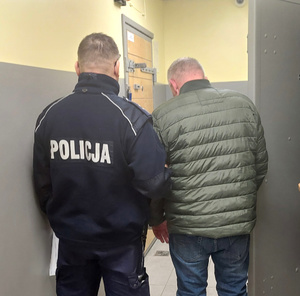 Policjant prowadzi zatrzymanego do celi