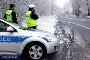Policjanci przy radiowozie na drodze w zimowych warunkach