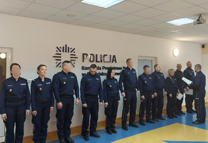 Grupa policjantów w rzędzie, komendant wręcza listy gratulacyjne