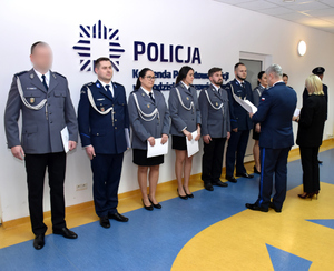 Grupa policjantów stoi w szeregu, komendant wręcza dokument jednemu z nich