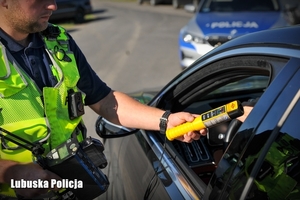 Ręka policjanta podczas sprawdzania trzeźwości kierowcy, z tyłu radiowóz