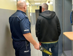 Policjant prowadzi zatrzymanego do celi