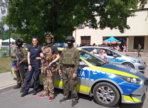 Policjantka z uczestnikami pikniku w wojskowych mundurach przy radiowozie