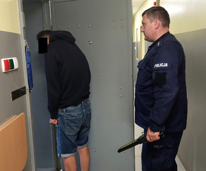 policjant prowadzi zatrzymanego do celi