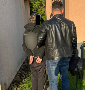 Zatrzymana osoba w kajdankach z policjantem służby kryminalnej przed budynkiem