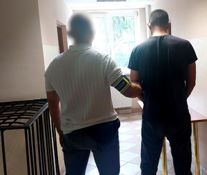 policjant kryminalny prowadzi zatrzymanego korytarzem komendy