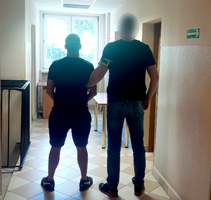 Policjant kryminalny prowadzi zatrzymanego korytarzem komendy