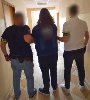 Dwóch policjantów w cywilnym ubraniu prowadzi zatrzymanego korytarzem komendy