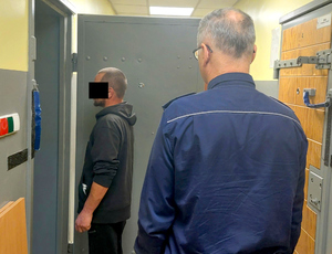 Policjant prowadzi zatrzymanego mężczyznę do celi